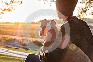 Hugging a dog in beautiful nature at sunset. Woman facing evening sun sits with her pet next to her and enjoys beauty of nature