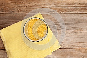 Hulled millet in bowl on wooden background, top view. Yellow grain. Rustic style photo