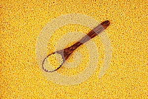 Hulled millet in a wooden spoon, top view. Yellow grain as background, copy space photo