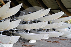 Hulls of school sailboats racked one above another on two levels in a dry rack boat storage facility in winter season