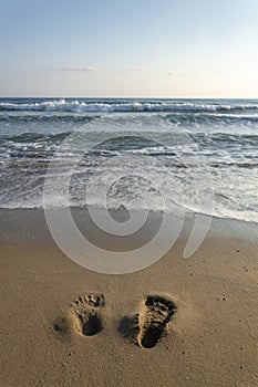 Human barefoot footprints in sand heading to sea awaiting incoming wave