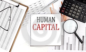 HUMAN CAPITAL text on notebook with clipboard and calculator on a chart background