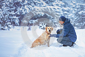 A human and a dog are best friends. The man with the dog sits in a snowy field in winter