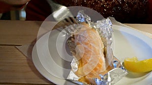 Human eats salmon baked in foil with a fork in a restaurant or cafe.