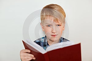 Human face expressions and emotions. Children and education. A close-up of attractive little boy with fair hair reading a book bei