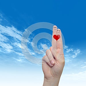 Human or female hands with two fingers painted with a red heart and smiley faces over cloud blue sky