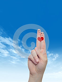 Human or female hands with two fingers painted with a red heart and smiley faces over cloud blue sky