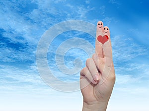 Human or female hands with two fingers painted with a red heart and smiley faces over cloud blue sky