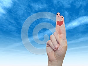 Human or female hands with two fingers painted with a red heart and smiley faces over cloud blue sky