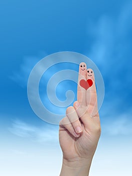 Human or female hands with two fingers painted with a red heart and smiley faces over cloud blue sky