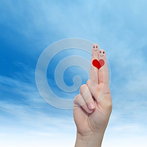 Human or female hands with two fingers painted with a red heart and smiley faces over cloud blue sky