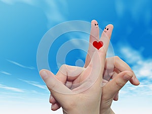 Human or female hands with two fingers painted with a red heart and smiley faces over cloud blue sky