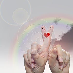 Human or female hands with two fingers painted with a red heart and smiley faces over rainbow sky background