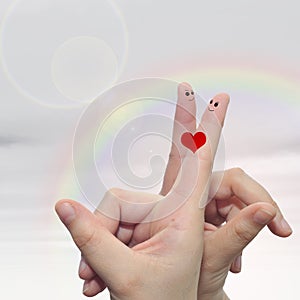 Human or female hands with two fingers painted with a red heart and smiley faces over rainbow sky background