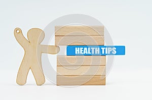 A human figurine pushes a blue wooden block labeled - HEALTH TIPS from a wall of blocks