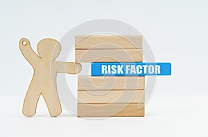 A human figurine pushes a blue wooden block labeled - RISK FACTOR from a wall of blocks
