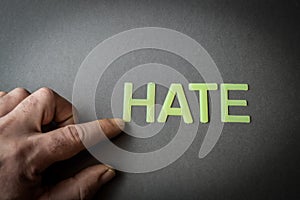 Human finger pointing the word Hate written with plastic letters on dark gray paper background