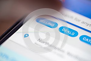 Human finger thumb over Deals button icon on shopping app on smartphone screen closeup