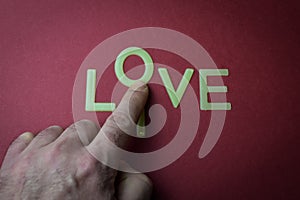 Human fingers sliding a letter to the word Live to make it Love, written with plastic letters on a dark red paper background