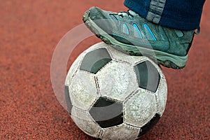 Human foot in a dirty sneaker on an old soccer ball