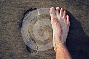Human footprint with barefoot feet in brown yellow sand beach background, active healthy living and personal growth concept
