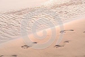 Human footprints in the sand close-up at sunrise. Pastel background.
