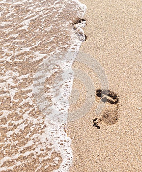 Human footprints on the sand with sea water. Foam from a wave on the sand with traces.