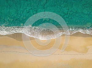 Human footprints on a sandy shore along the sea with breaking waves, aerial view directly above