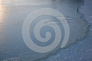 Human footprints visible beneath thin ice on frozen lake surface in cold winter