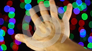 Human hand on beautiful blurred background of meteoric multicolored garland