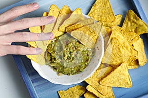 Human hand grab nachos corn chips with guacamole sauce close up photo