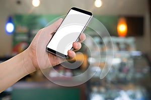 Human hand hold smart phone, tablet, cellphone with white blank screen on blurry coffee shop Background.