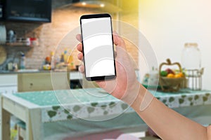 Human hand hold smart phone, tablet, cellphone with white blank screen on blurry Kitchen room Background.