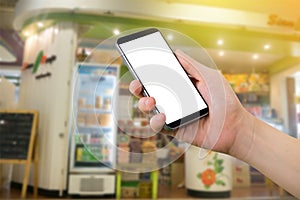 Human hand hold smartphone with blank screen on blurry snack shop background.