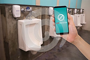 human hand hold smartphone, ell phone with blank screen on blurry row of urinal at public restroom.