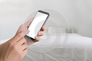 Human hand hold and touch smartphone on blurry bedroom background.
