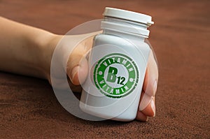 Human hand holding a bottle of pills with vitamin B12