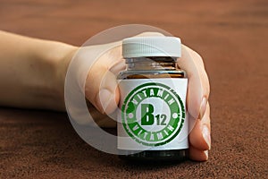 Human hand holding a bottle of pills with vitamin B12