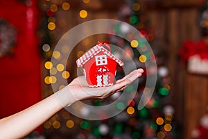 Human hand holding decorative red house against blurred background. Christmas and home comfort concept.