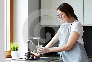 Human hand holding glass pouring fresh drink water at kitchen faucet