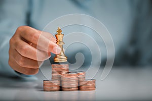 Human hand holding gold king chess on stack of coins, money power or saving money, financial growth, business finance wealth and