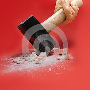 Human hand holding hammer broke rock and smashed it in pieces.Red background