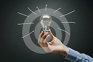 Human hand holding light bulb on dark background, business idea concept, creativity