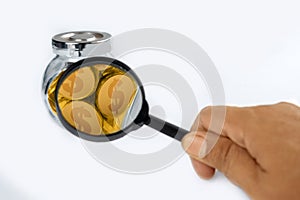 A human hand holding a magnifying glass and focusing on golden coins inside glass jars