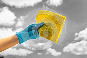 Human hand holding napkin for cleaning window on grey background. A female hands in bright blue gloves washes the windows