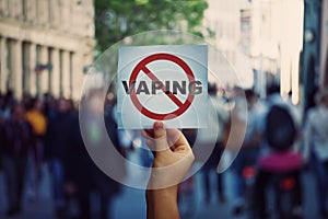 Human hand holding a protest banner stop vaping message over a crowded street background. Banning flavored vaping products to photo