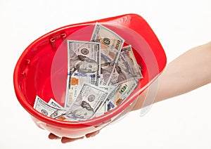 Human hand holding a red hard hat with money