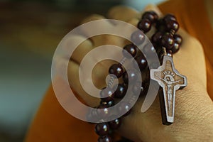 Human hand holding a rosary on the shoulder closeup. Junior young man hands praying holding a rosary with Jesus Christ Cross or