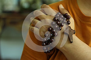 Human hand holding a rosary on the shoulder. Junior young man hands praying holding a rosary with Jesus Christ Cross or Crucifix.