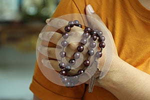 Human hand holding a rosary on the shoulder. Junior young man hands praying holding a rosary with Jesus Christ Cross or Crucifix.